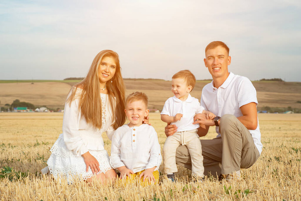 Parents with small sons sit among field and rest smiling - Photo, Image