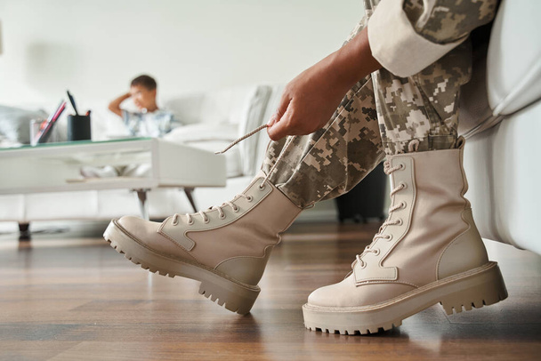 Femme portant uniforme militaire attacher ses lacets de chaussures tout en étant assis sur le canapé - Photo, image