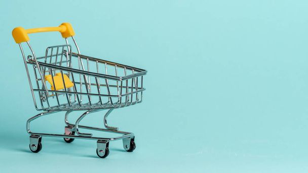 Shopping cart on blue background. Shop trolley at supermarket as sale, discount, shopaholism concept with copy space for text or design. - Photo, image
