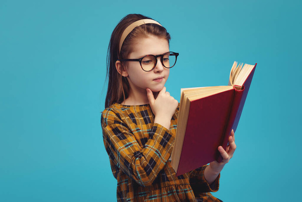 Happy schoolgirl in eyeglasses reading book and doing homework  - Φωτογραφία, εικόνα