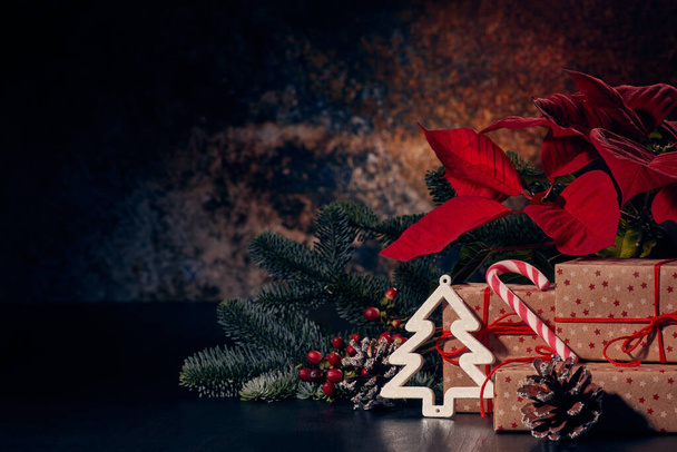 Christmas decoration with Red Poinsettia flowers (Euphorbia Pulcherrima), fir branch and gift boxes on a dark background. New year and Christmas background with copy space. Greeting card. - Fotoğraf, Görsel
