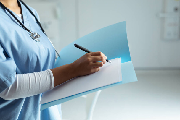 La mitad de la sección de raza mixta médico femenino escribiendo en un archivo en el hospital - Foto, Imagen