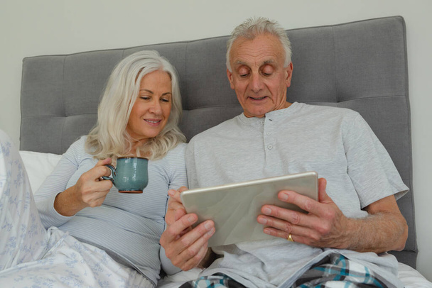 Frontansicht eines aktiven Senioren-Paares mit digitalem Tablet im heimischen Schlafzimmer - Foto, Bild