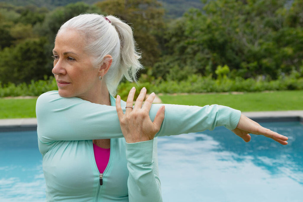 Side view of active senior Caucasian woman exercising near poolside in the backyard of home - Photo, Image