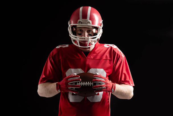Porträt eines selbstbewussten amerikanischen Fußballspielers mit Helm auf schwarzem Hintergrund - Foto, Bild