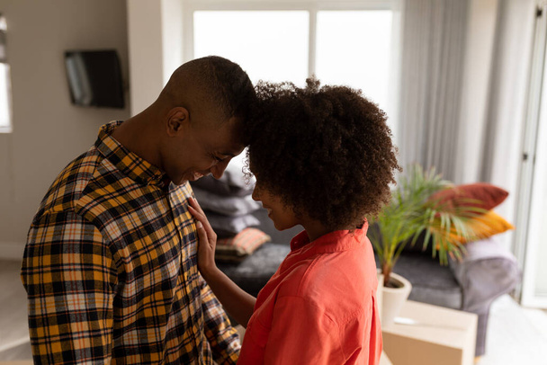 Side view of romantic young mixed-race couple looking at each other head to head in living room at home. - Photo, Image
