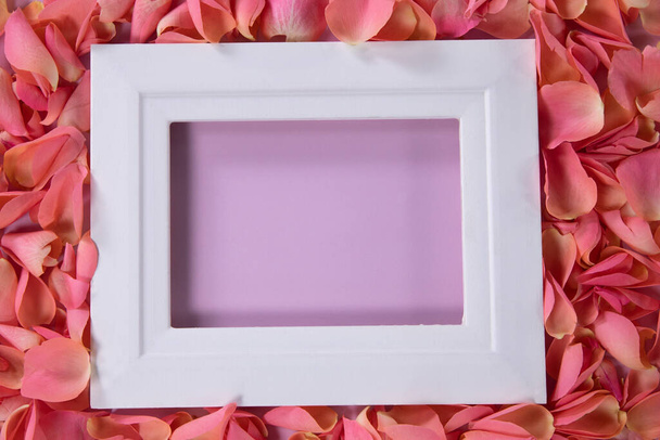 Close-up of a white empty photo frame with a pink background surrounded by pink rose petal for valentines day - Foto, Bild
