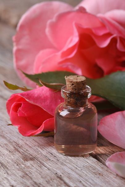 Рожева вода в скляній пляшці на фоні рожевих троянд
 - Фото, зображення