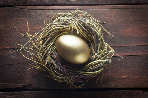 golden egg in a nest on a wooden background - Foto, imagen