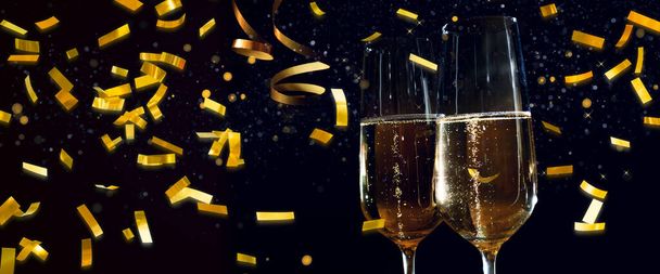 Champagne glasses and golden confetti in front of dark night sky. Background for a holiday concept. - Photo, image