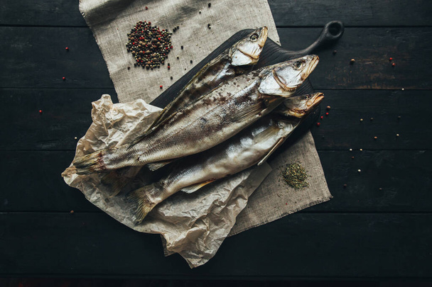 delicious beautiful fresh dried wild sea river red and white fish on a wooden brown dark board on paper on a linen cloth cloth pike, bream, ram, mackerel, herring, with spices stylish beautiful color combination on a dark background on a wooden table - Photo, Image