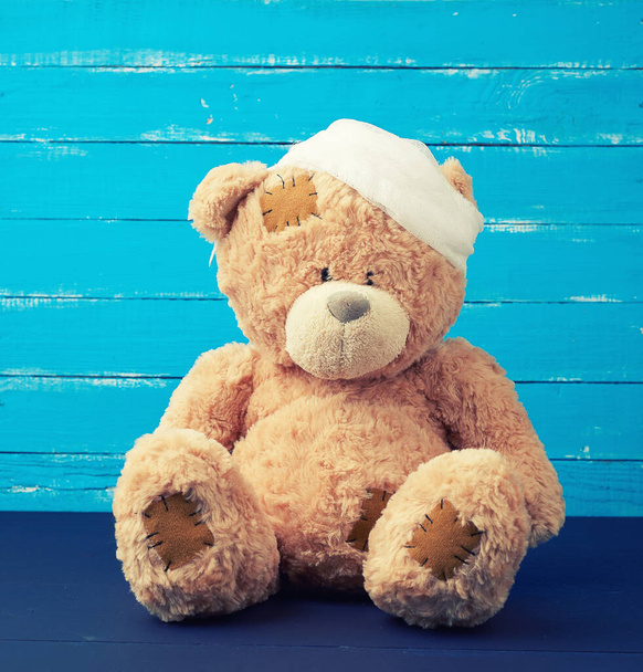sad brown bear sits with bandaged white medical bandage head, injury and headache concept - Photo, Image