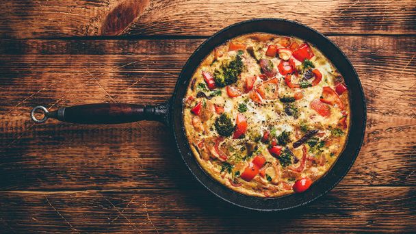 Vegetable frittata with broccoli, red bell pepper and red onion in cast iron skillet. View from above - Foto, Bild
