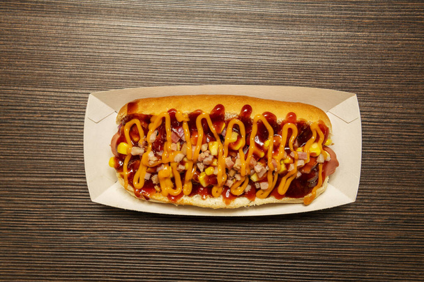Imagen de vista superior de hot dog con ketchup, tacos de jamón frito, maíz dulce, salsa de queso cheddar dentro de una bandeja de cartón - Foto, imagen