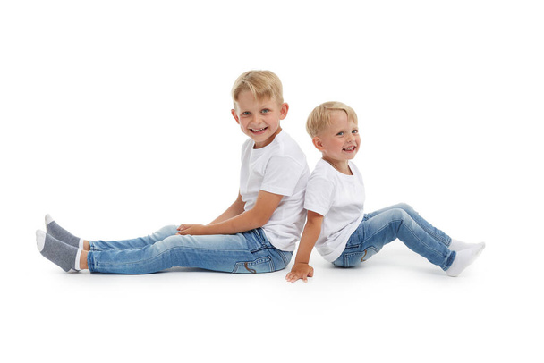 Friendly family. Older brother and younger boy are sitting with backs to each other isolated on a white background. Happy siblings. Two little brothers. Concept of people and family - Photo, Image