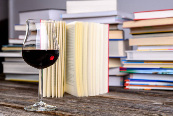 book and wine glass in front of piles of different books on wooden table - Foto, Bild