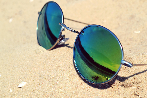 Spiegelnde Sonnenbrille auf Sand mit Spiegelung des Strandes - Foto, Bild