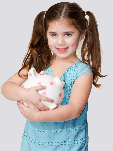 Cute little girl cradles a pink polka dotted piggybank in arms. - Foto, afbeelding
