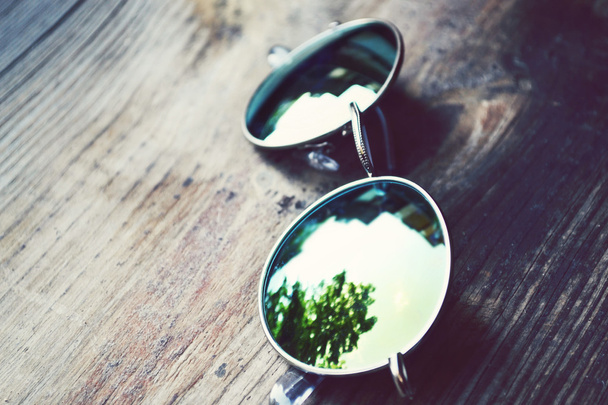 okulary przeciwsłoneczne leżące na drewnianym stole z odbiciem drzew - Zdjęcie, obraz