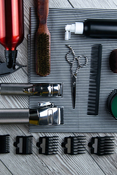 Flat lay from hairdressing accessories including: haircuts, scissors, combs, gels for styling and shaving laid out on a striped towel that stands on a wooden table. Top views - Fotoğraf, Görsel