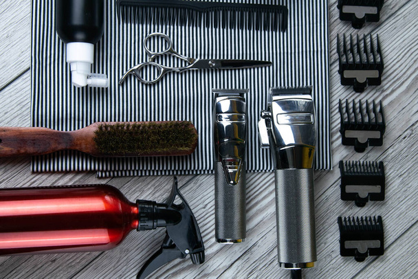 Plancha plana de accesorios de peluquería que incluyen: cortes de pelo, tijeras, peines, geles para el peinado y afeitado dispuestos en una toalla a rayas que se encuentra en una mesa de madera. Top vistas
 - Foto, Imagen
