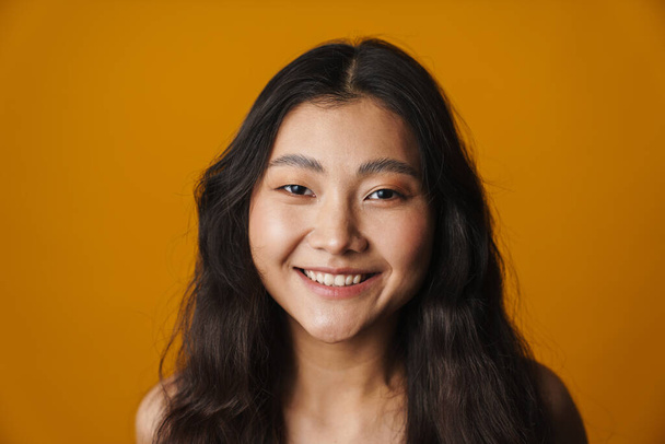 Close up of a smiling young asian woman with long brunette hair standing over yellow background looking at camera - Fotoğraf, Görsel