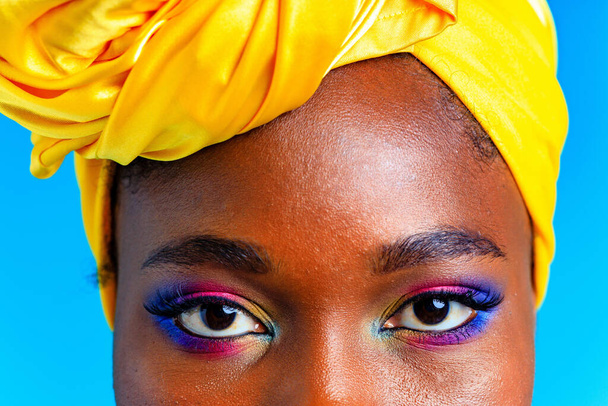 close up shot of female eyes rainbow make-up and long eyelashes with turban over head in blue studio baclground - Фото, изображение