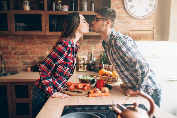 Happy couple kissing while preparing a romantic dinner. Vegetable salad preparation. Family prepares healthy food on the kitchen - Zdjęcie, obraz