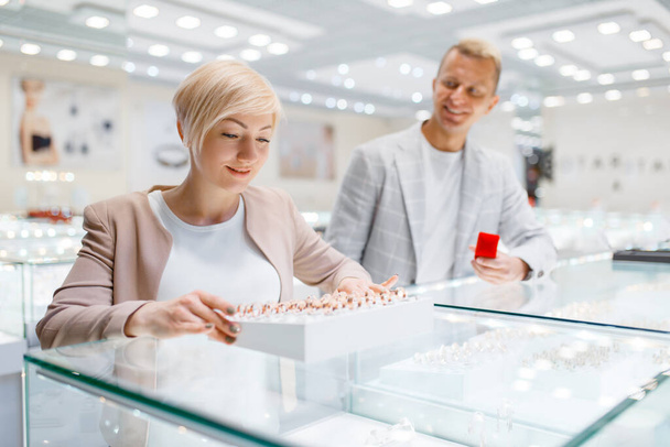 Happy love couple purchase wedding rings in jewelry store. Man and woman choosing gold decoration. Future bride and groom in jewellery shop - 写真・画像