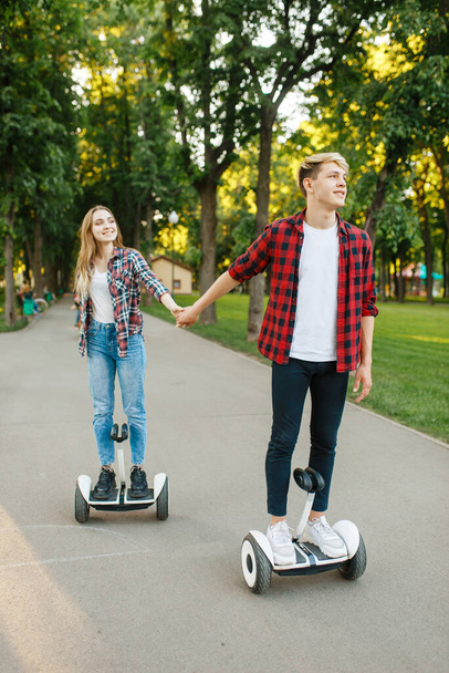 Young couple riding on gyro board in park. Outdoor recreation with electric gyroboard. Transport with balance technology - Photo, image