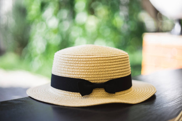 Шляпа на столе. Соломенная шляпа с черной лентой. Концепция отдыха и отпуска. Стол в кафе в парке. Солнечная жаркая погода. - Фото, изображение