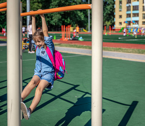 A little girl, an elementary school student, plays on the playground after school, pulls herself up on a horizontal bar. - Photo, image