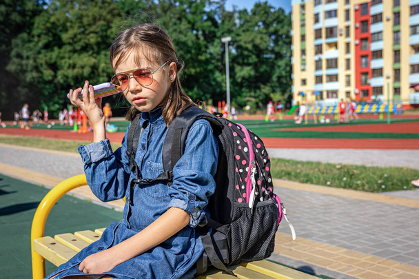 Une petite fille, une élève du primaire en lunettes de soleil téléphonant, parlant, communiquant. - Photo, image