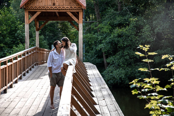 Όμορφο νεαρό ζευγάρι φιλιέται σε μια γέφυρα στο δάσος, μια ημερομηνία στη φύση, ιστορία αγάπης. - Φωτογραφία, εικόνα