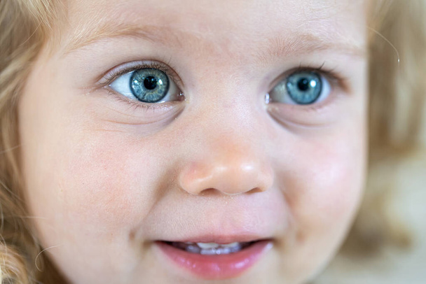 Κοντινό πλάνο πρόσωπο ενός μικρού χαριτωμένου κοριτσιού με μεγάλα μπλε μάτια. - Φωτογραφία, εικόνα