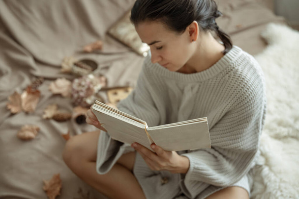 Jolie jeune femme en pull tricoté confortable lisant un livre au lit. - Photo, image