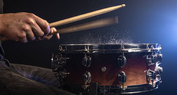 Baterista usando bastões de tambor batendo tambor snare com água espirrando no fundo preto sob iluminação estúdio de perto. - Foto, Imagem