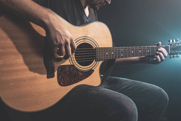 Close-up van een man die in het donker akoestische gitaar speelt met podiumverlichting. - Foto, afbeelding