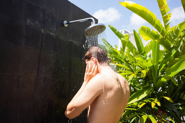 Man washing ears while taking shower on sunny day. - 写真・画像