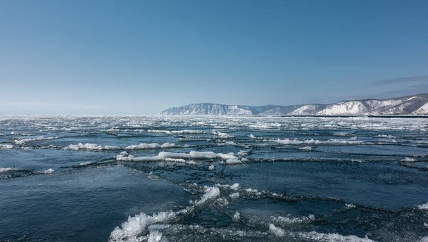No início da primavera. Uma deriva de gelo começa no lago. Rachaduras e neve derretida são visíveis na superfície azul. Uma cordilheira contra um céu azul claro. Baikal. - Foto, Imagem
