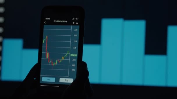 Auf dem Bildschirm des Mobiltelefons in der Anwendung werden Diagramme der Wertänderungen von Kryptowährungen angezeigt. Vor dem Hintergrund animierter Grafiken - Filmmaterial, Video