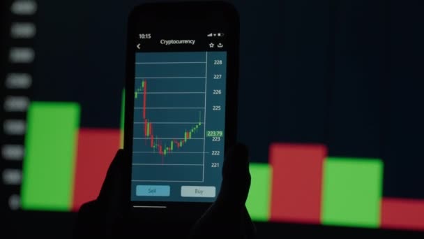 携帯電話で手、株式市場のデータをチェックします。携帯電話の株式交換。背景にあるグラフと表 - 映像、動画