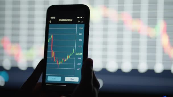 携帯電話で手、株式市場のデータをチェックします。携帯電話の株式交換。背景にあるグラフと表 - 映像、動画