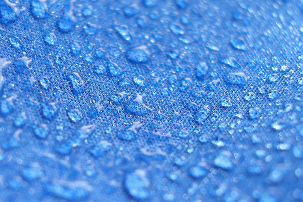 Water drops on the fabric. Rain Water droplets on blue fiber waterproof fabric. Water drops pattern over a waterproof cloth. Blue background. - Photo, Image