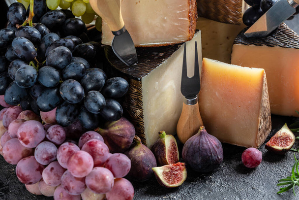 Çeşitli peynir türleri. Üzüm ve incir ile. Peynir bıçağıyla kompozisyon. Geleneksel İspanyol, Fransız, İtalyan peyniri parçaları. - Fotoğraf, Görsel