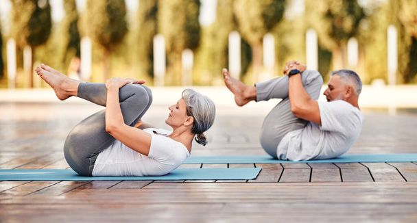 Active mature family man and woman doing yoga exercise  lying on mat hugging her knees to chest after yoga practice outdoor in park, healthy active senior couple doing stretching exercises in morning    stretching back  - Zdjęcie, obraz