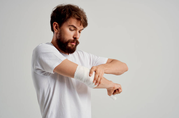 homme malade dans un T-shirt blanc avec une main bandée posant la médecine de l'hôpital - Photo, image