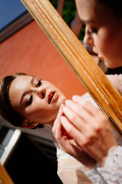 a beautiful young woman in a lace robe looks at her reflection in the mirror. - Fotografie, Obrázek