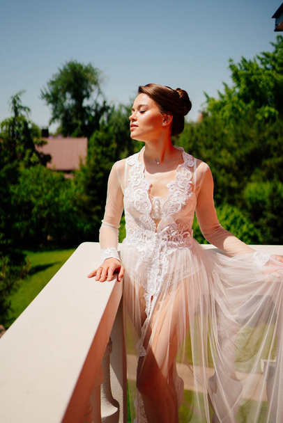 a beautiful bride in a transparent lace robe stands on the terrace.  - Foto, immagini