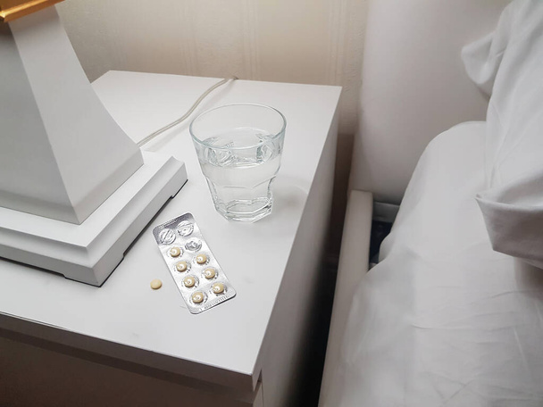 Крупним планом спальні таблетки і склянка води, приготована для спокійного і здорового сну на тумбочці в спальні, концепція здоров'я і хвороб
 - Фото, зображення